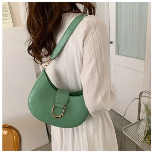 Detail of green crocodile texture hobo bag with gold metal buckle shown on a shoulder