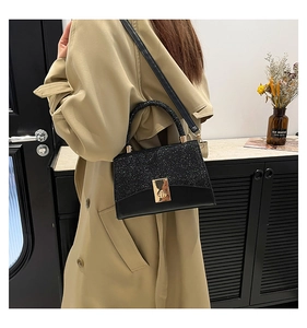 Detail of black sequined crossbody bag featuring a golden twist lock and leather strap
