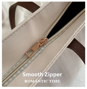 Detail of smooth gold zipper hardware on beige pebbled leather tote with brown handle