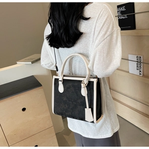 Detail of two-tone tote bag with black textured body and white leather handles worn by model