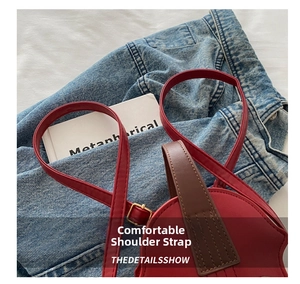 Detail of red leather shoulder strap and gold buckle on a stylish crossbody bag