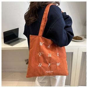 Close-up of orange corduroy tote bag with white fashion embroidery on a model