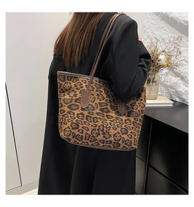 Leopard print tote bag with brown leather straps shown on shoulder in a minimalist room