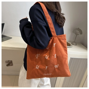 Detail of orange corduroy tote bag featuring white embroidered 'Future' text and texture
