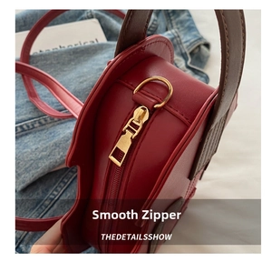 Detailed close-up of smooth gold-tone zipper and hardware on red leather shoulder bag