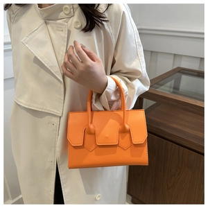 Détail d'un sac à main orange vif avec rabat minimaliste et anses lisses sur un trench