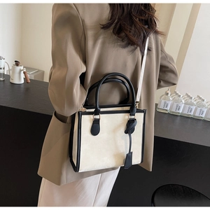 Detail of beige minimalist tote bag with black trim and detachable shoulder strap on model