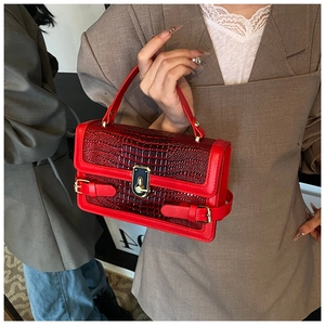Detail of red crocodile pattern handbag with golden turn-lock and buckle decorations