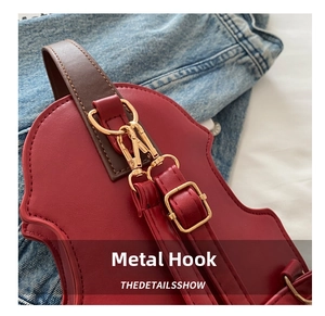 Close-up of bright gold hardware hooks and dark brown leather strap on a red saddle bag