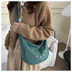Détail du sac bandoulière en velours côtelé vert foncé avec logo blanc circulaire