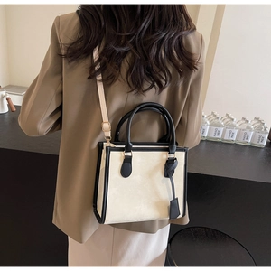 Detail of a contrast-color tote bag in cream PU leather with black handles and shoulder strap
