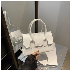 Détail d'un sac à main en cuir blanc avec fermeture à rabat sur une surface métallique