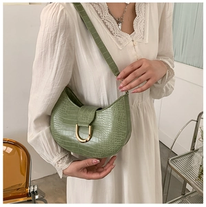 Detail of green crocodile textured crescent bag with golden U-shaped buckle on white lace dress