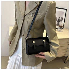 Détail d'un sac bandoulière noir carré avec boucles dorées sur la sangle réglable