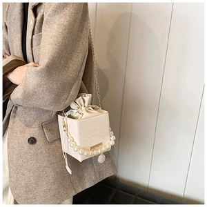 Detail of a chic cream lace bucket bag with pearl handle and golden chain on tweed blazer