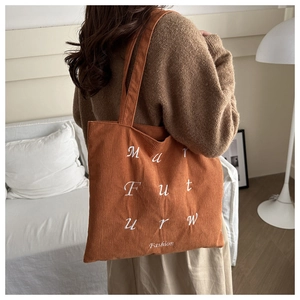 Detail of orange corduroy tote bag with white letter embroidery shown on shoulder