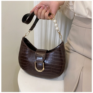 Detail of dark brown crocodile pattern handbag with gold horseshoe buckle and pearl strap