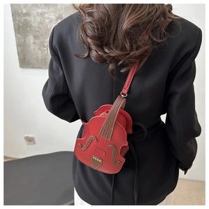 Creative red violin-shaped crossbody bag with gold rivet details on black suit model