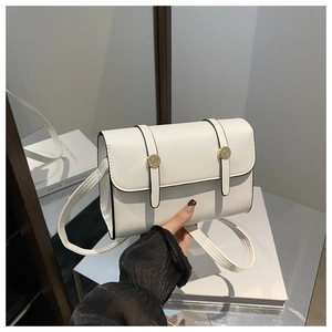 Détail d'un sac bandoulière blanc minimaliste avec boucles dorées et bords noirs