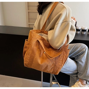Detail of orange corduroy tote bag showing ribbed texture, metal snap, and side pocket