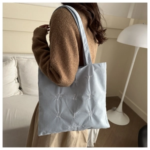 Detail of light blue corduroy tote bag featuring white embroidered letters and soft texture