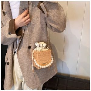 Detailed shot of brown lace textured bucket bag with pearl handle and golden chain