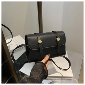 Détail d'un sac à bandoulière carré noir mat avec des boucles dorées et rabat élégant