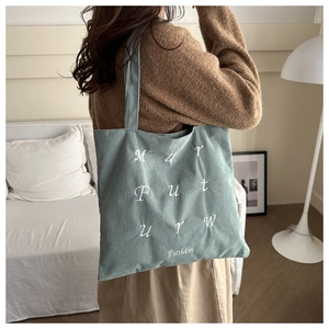 Close-up of light teal corduroy tote bag with white embroidery on a model