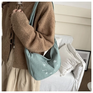 Close-up of green corduroy crescent tote bag with white letter print on a model