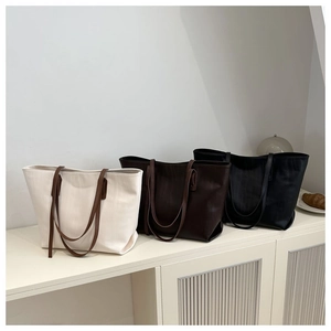 Three large minimalist tote bags in cream, brown, and black displayed on a white shelf