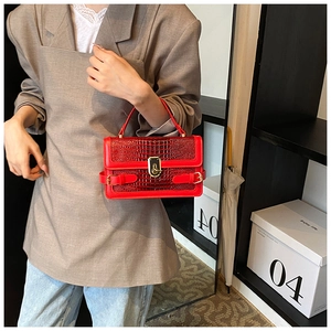 Detail of red crocodile pattern PU leather handbag with elegant gold metal clasp and belt