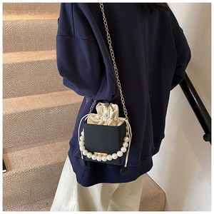 Detail of black box bucket bag with pearl handle, gold chain and cream drawstring closure