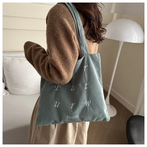 Detailed close-up of light blue corduroy tote bag with white embroidered lettering