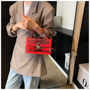Detail of red crocodile pattern handbag featuring a classic gold lock and metal buckles