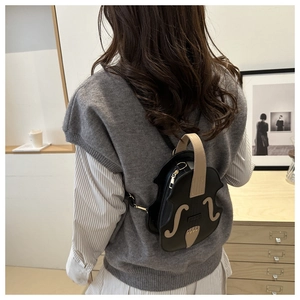 Detail of creative violin shaped crossbody bag in black finish worn by a model in a room