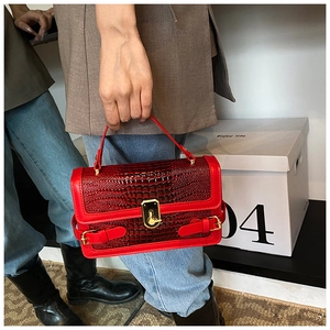 Detail of red crocodile texture handbag featuring a golden turn-lock and elegant handle
