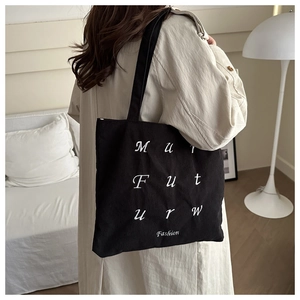 Detail of black corduroy tote bag showing white embroidered lettering and long shoulder strap