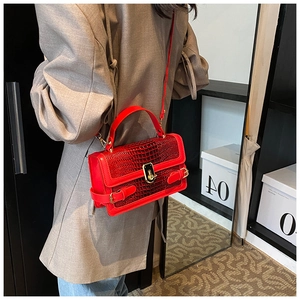 Detail view of red crocodile textured bag with gold clasp shown on a model
