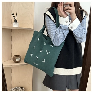 Detail of dark green corduroy tote bag featuring white embroidered fashion lettering