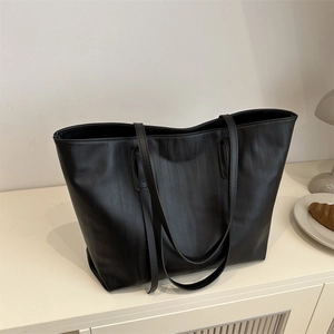 Minimalist black tote bag with vertical wavy texture and long straps on a white cabinet