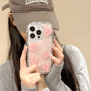 Coque iPhone rose nacré avec cœurs 3D et bords ondulés transparents tenue par un modèle