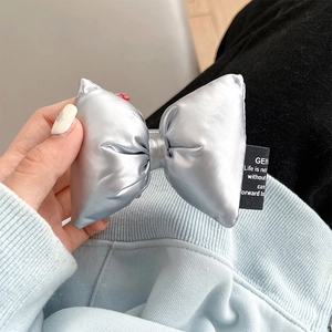 Detailed view of silver puffy bow accessory with metallic leather and fabric label