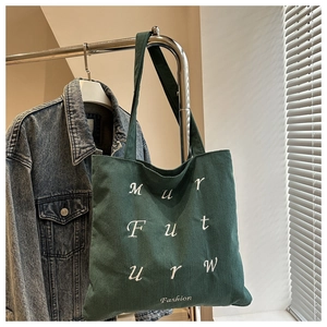 Detail of dark green corduroy tote bag featuring white embroidered fashion lettering