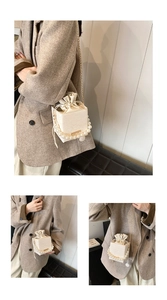 Detail of cream white pearl handle bucket bag with lace pattern and gold chain strap