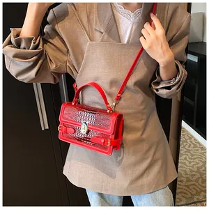 Detailed view of red crocodile pattern crossbody bag with golden metal twist lock and strap