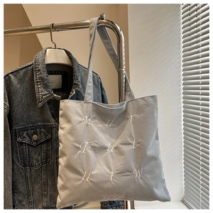 Detail of grey corduroy tote bag featuring white letter embroidery and soft texture