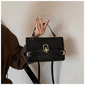 Detail of black crocodile texture bag with gold shield clasp held by a model