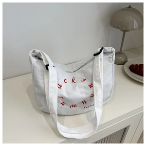Detailed shot of white corduroy bag featuring red letter embroidery and wide strap