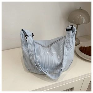 Close-up of light blue corduroy shoulder bag featuring white letter embroidery detail