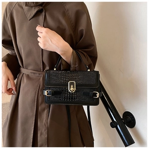 Detail of black crocodile pattern crossbody bag with gold twist lock on a staircase